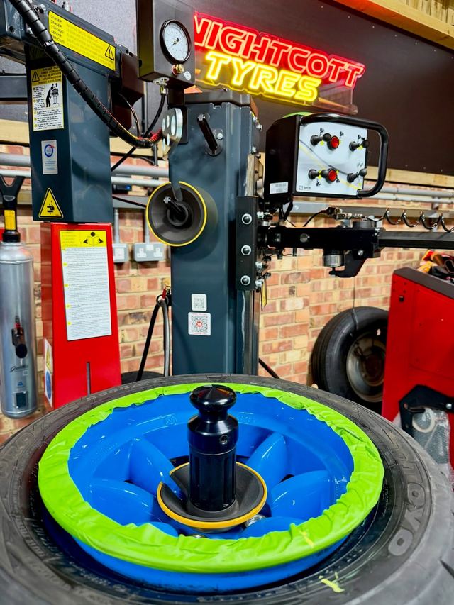 A wheel on the tyre changer under a blue and green rim protector