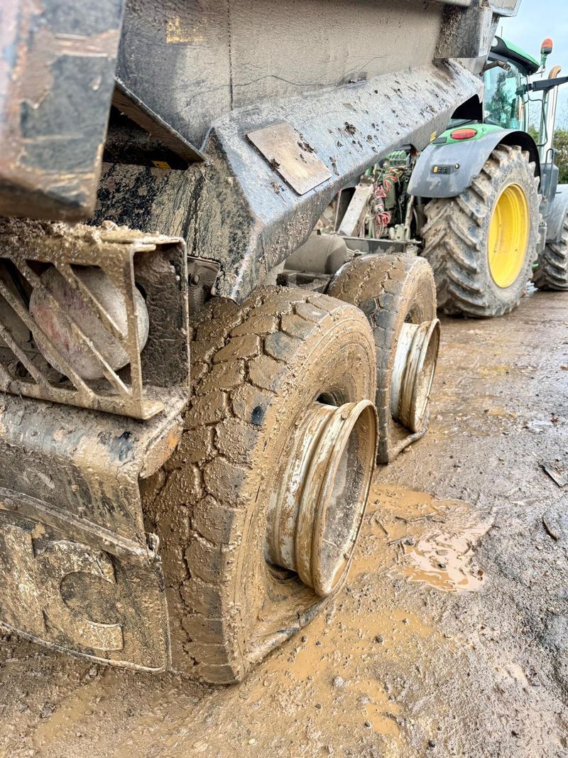 A tipping trailer's mud-caked wheels in a wet yard, the tyres flat around bare steel rims
