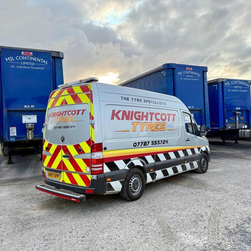 The silver Knightcott Tyres van parked among blue curtain-sided trailers at a haulage yard